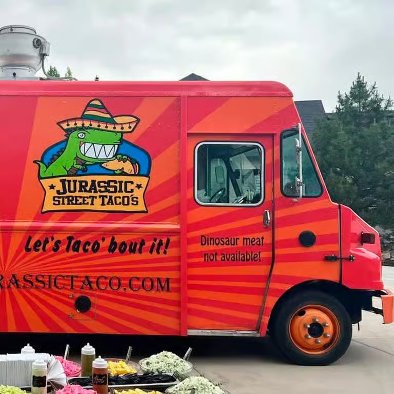 Jurassic Tacos food truck parked at a Utah catering event with a taco topping bar set up alongside